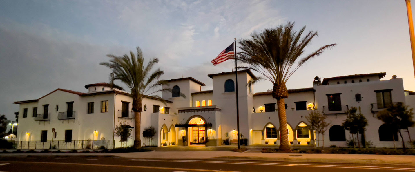 The exterior of Raya’s Paradise San Clemente glows at dusk with warm lighting, palm trees and a welcoming coastal atmosphere.