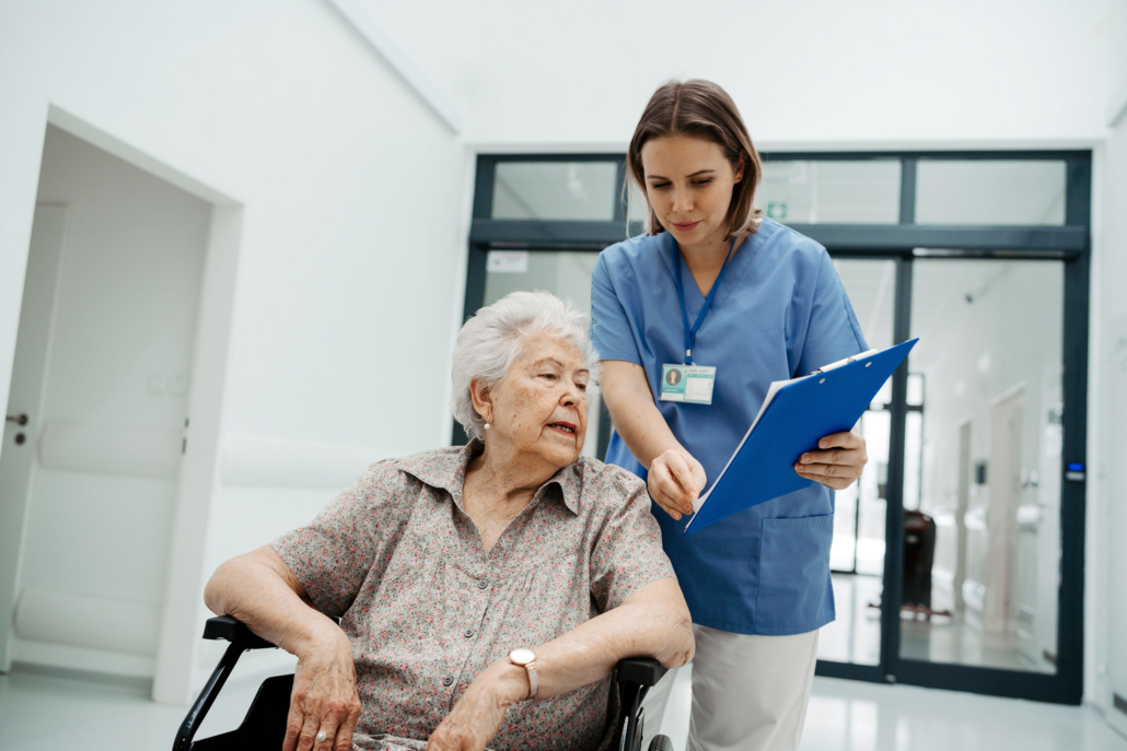 Healthcare worker reviews care documents with an older woman in a wheelchair during hospital discharge planning for assisted living.