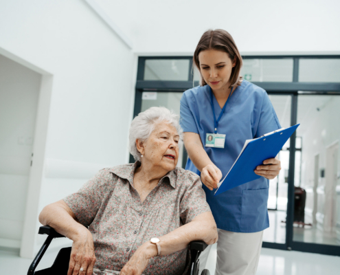 Healthcare worker reviews care documents with an older woman in a wheelchair during hospital discharge planning for assisted living.