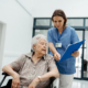 Healthcare worker reviews care documents with an older woman in a wheelchair during hospital discharge planning for assisted living.