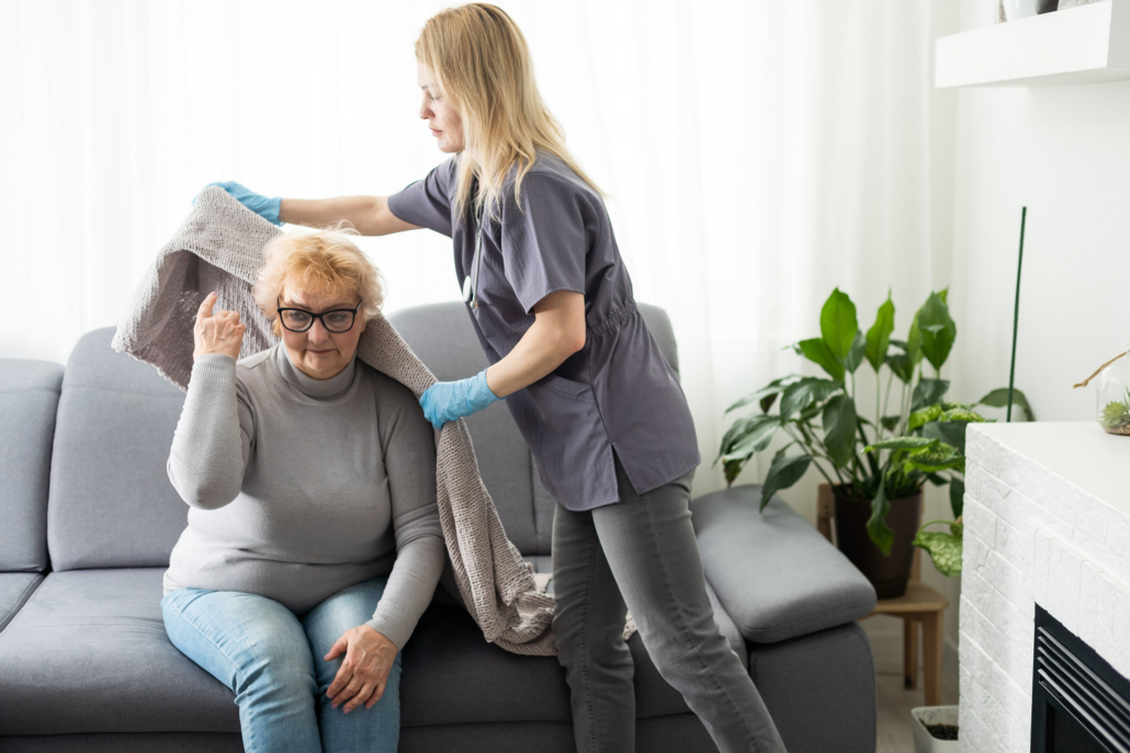 A professional caregiver helps an older woman with a blanket at home, illustrating personalized senior care and nursing home alternatives.