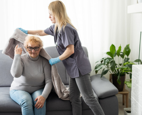 A professional caregiver helps an older woman with a blanket at home, illustrating personalized senior care and nursing home alternatives.