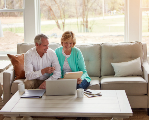 Older couple reviews documents and a laptop at home while exploring assisted living options and senior care transitions in California.