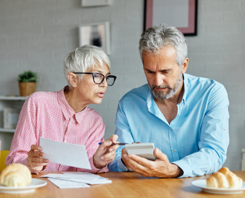 Older woman and man review paperwork and a calculator at home, discussing assisted living rate increases and notice requirements.