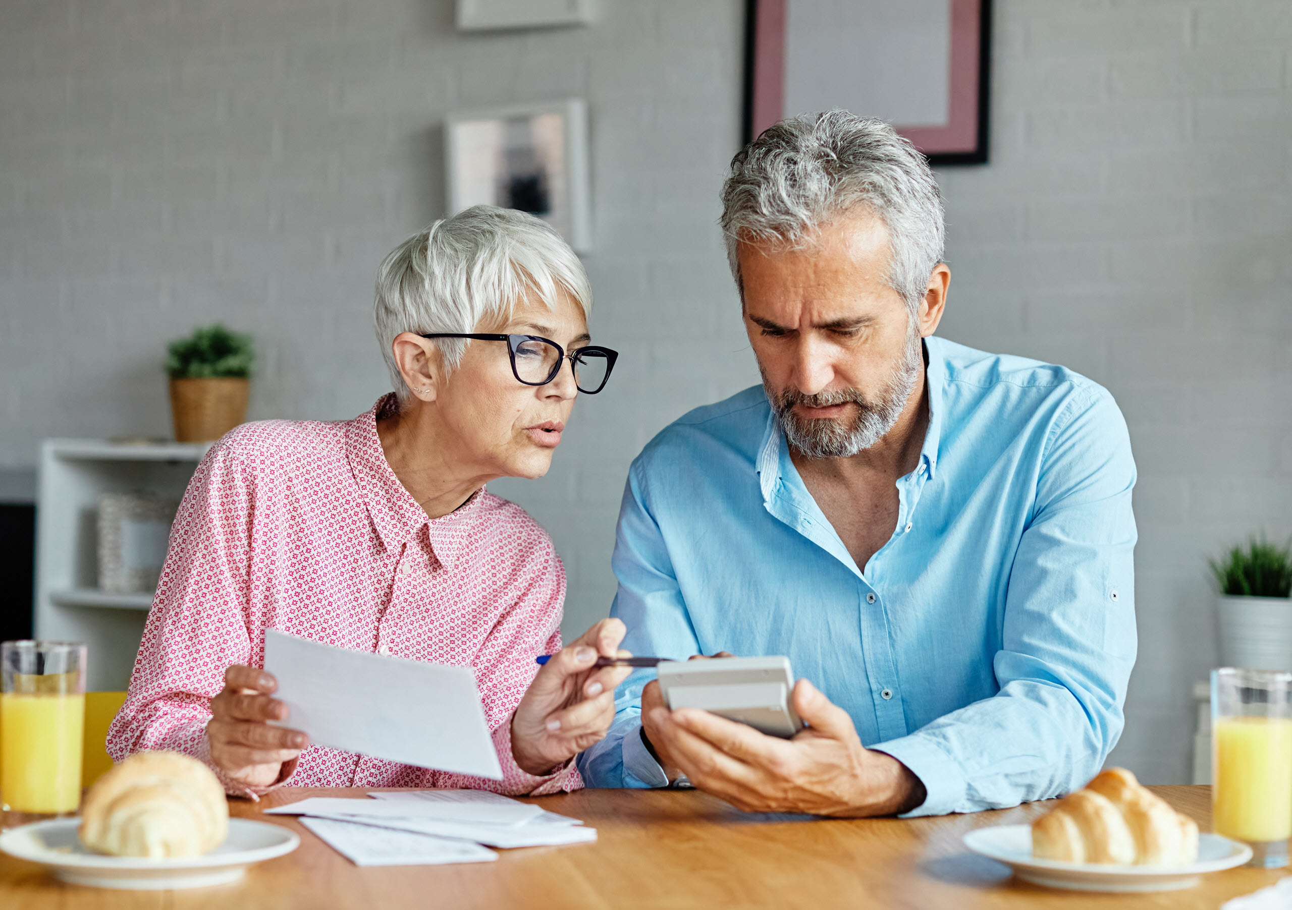 Senior Couple Reviewing Assisted Living Rate Increase Notice in California Older woman and man review paperwork and a calculator at home, discussing assisted living rate increases and notice requirements.