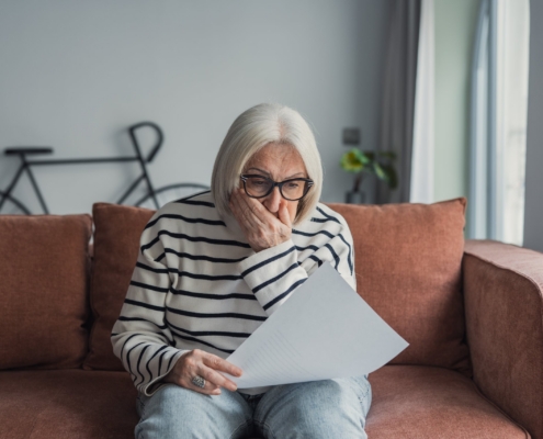 Older woman looks worried while reviewing paperwork at home, reflecting concerns about assisted living costs and financial uncertainty.