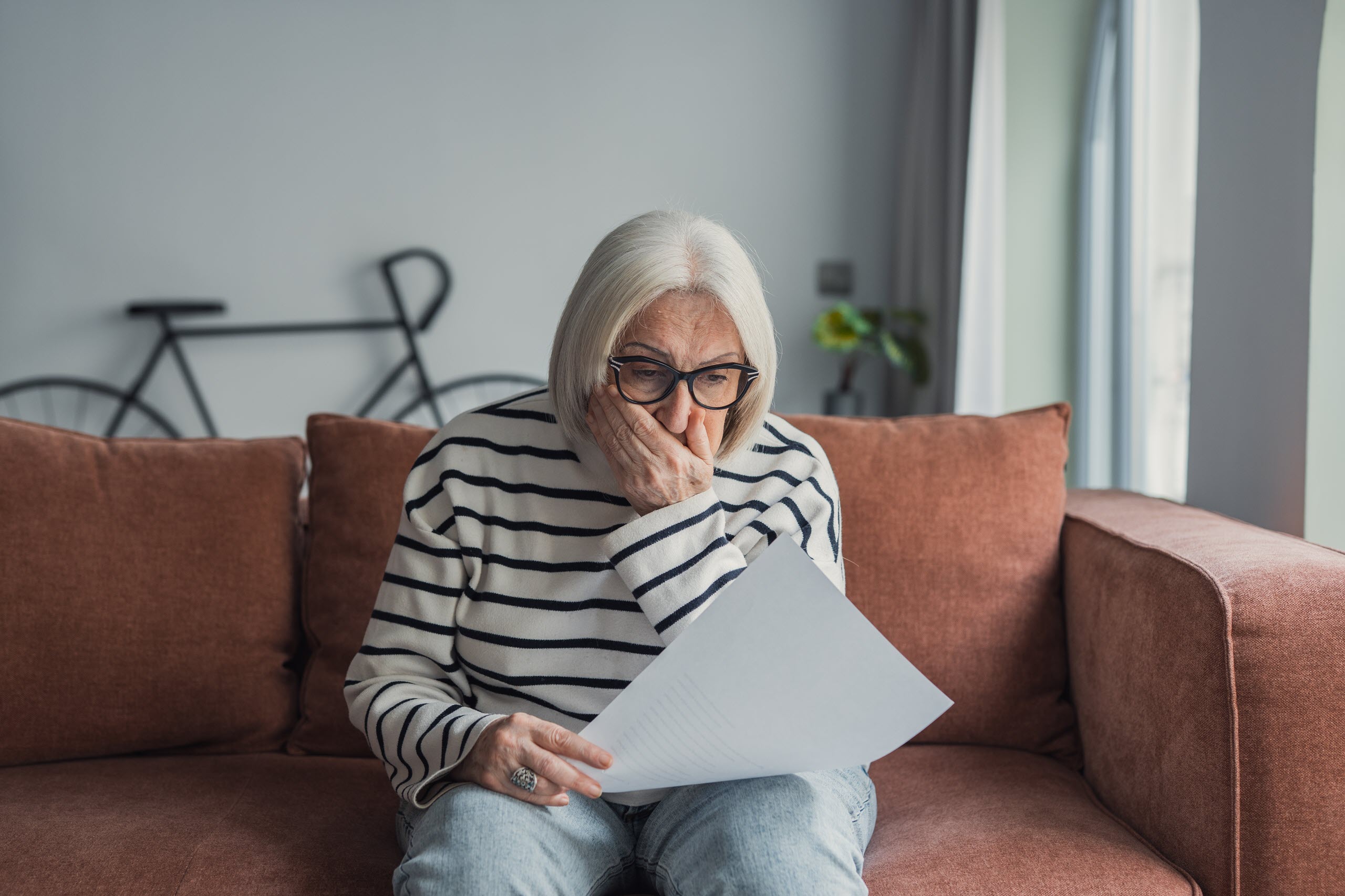 Older woman looks worried while reviewing paperwork at home, reflecting concerns about assisted living costs and financial uncertainty.